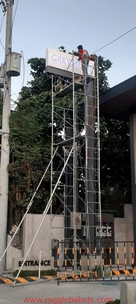 Billboard signage installation for GREY client in Ortigas, workers on scaffolding, tall pole near gate by M&G Global Ads.