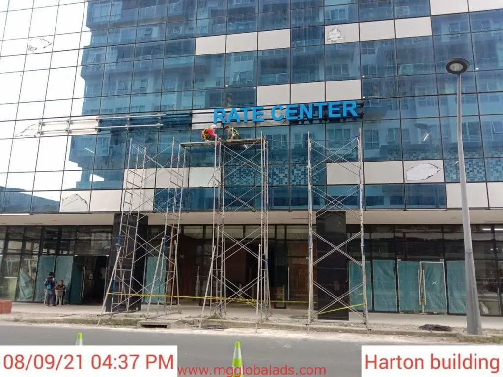 Outdoor building signage installation for RATE CENTER client, Harton, in Makati by M&G Global Ads. Workers and materials visible.