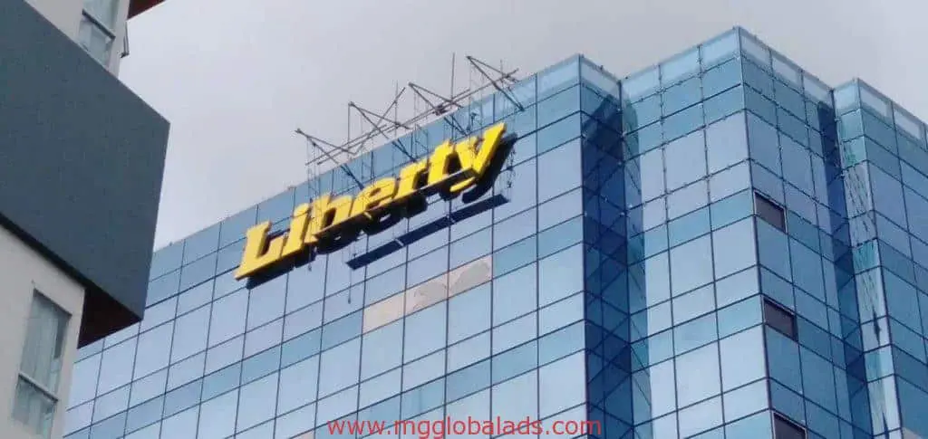 Liberty building metal sign in Makati on a modern glass office, overcast sky, architectural signage by M&G Global Ads.