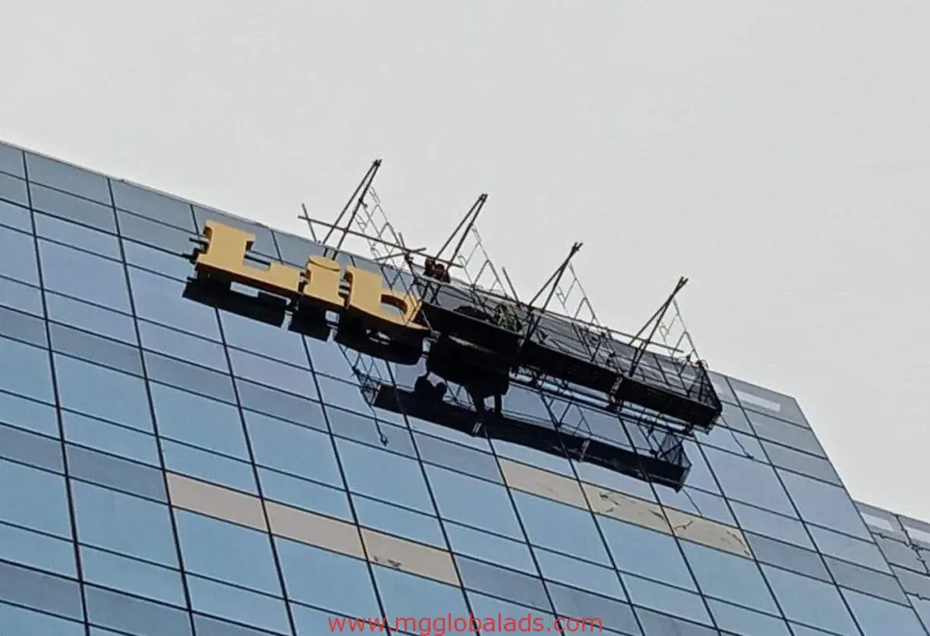 Building exterior acrylic signage installation for Lib client in Makati by M&G Global Ads; worker on platform, cloudy sky.
