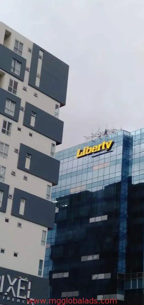 Glass office with Liberty yellow LED signage in Makati, beside modern residences, overcast sky by M&G Global Ads.