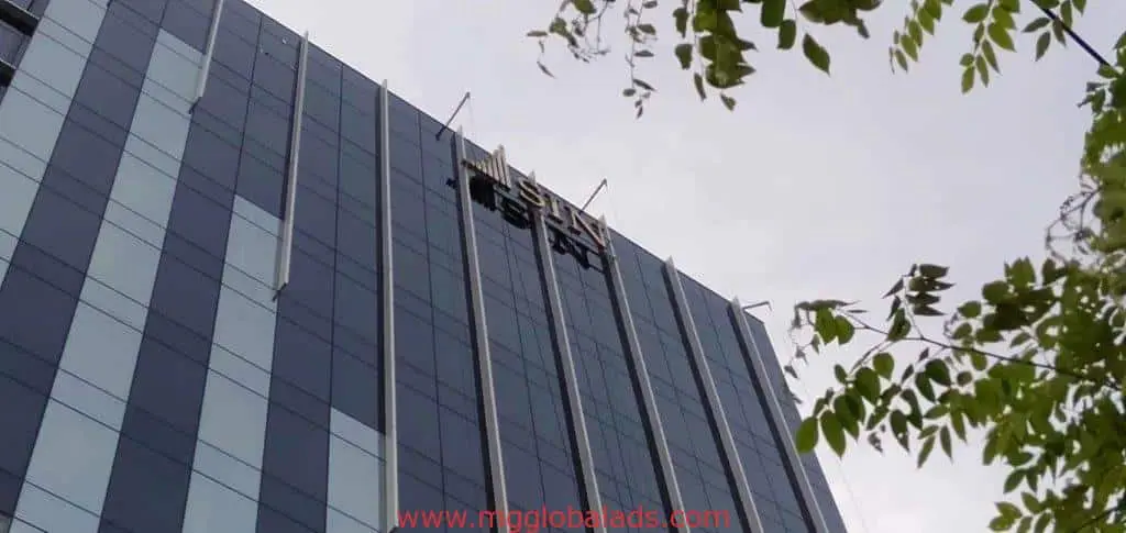 Workers cleaning windows on suspended scaffolding with sleek office building signage in BGC by M&G Global Ads.