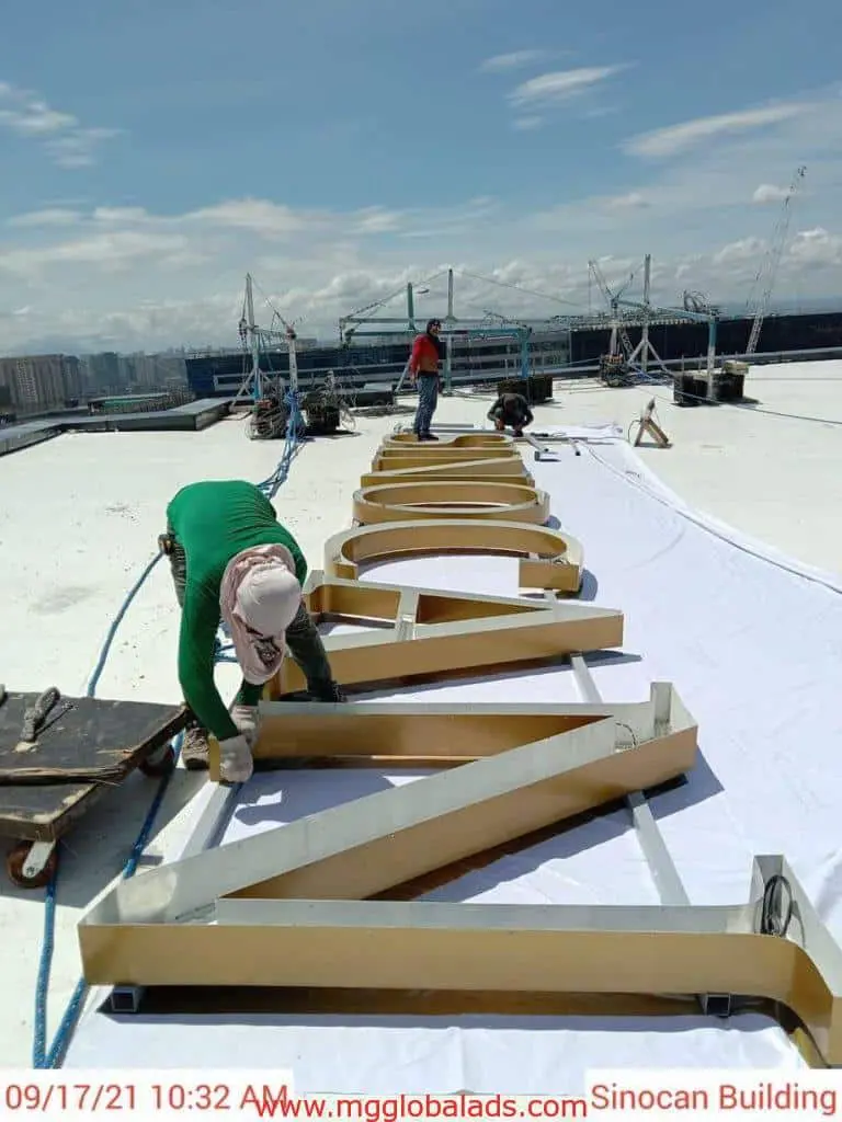 Installation of large metal channel letters signage for a client in Makati, with tools and cityscape visible, by M&G Global Ads.