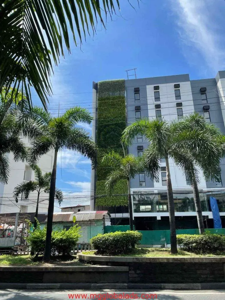 LED outdoor signage on a modern white building with a green wall in Makati, palm trees, blue sky—by M&G Global Ads.