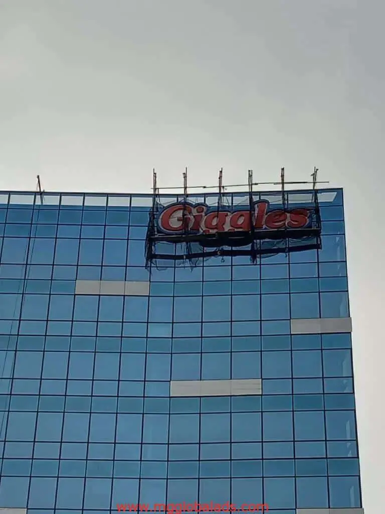 LED signage installation for Giggles on a glass building in Ortigas with scaffolding, cloudy sky—by M&G Global Ads.
