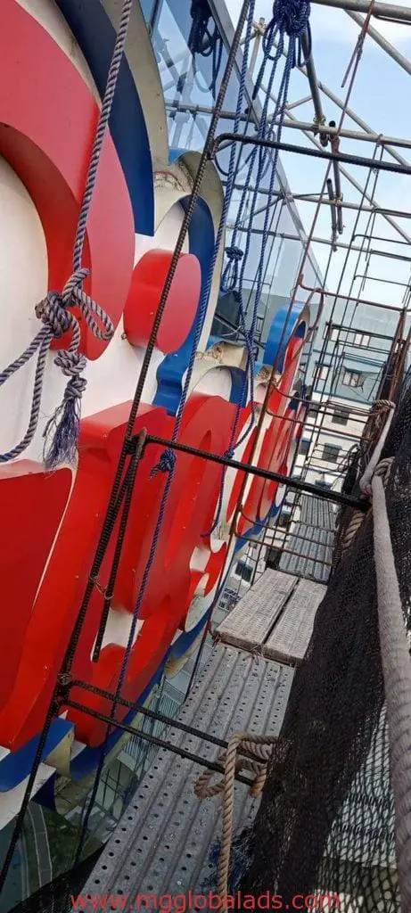 Billboard installation in Makati: view from scaffolding beside large red and white signage, safety gear visible, by M&G Global Ads.