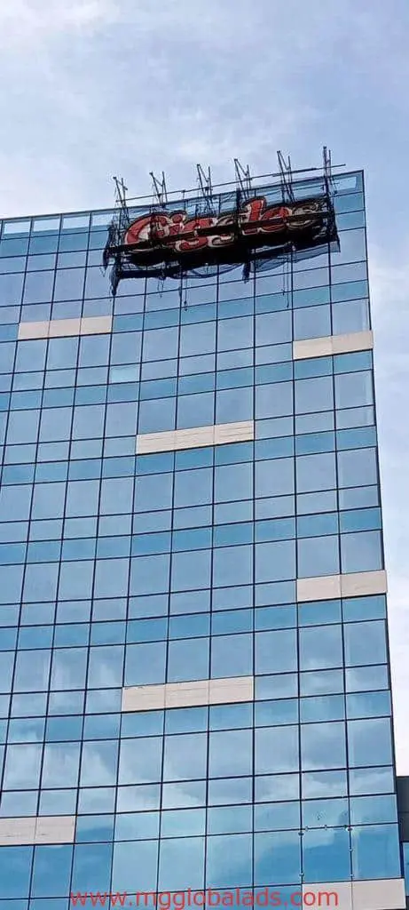 Damaged Coca-Cola rooftop signage on glass office building in Ortigas, blue sky background, by M&G Global Ads.