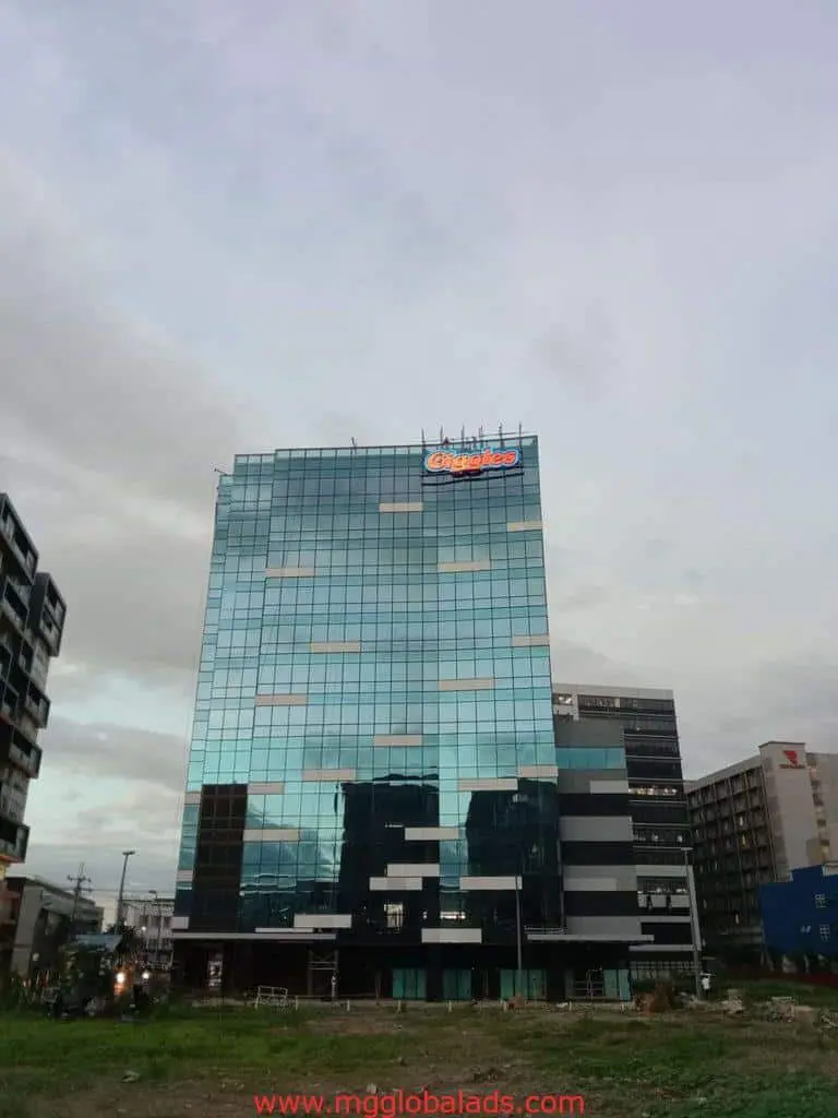 Office building with rooftop LED signage in Mandaluyong, surrounded by commercial structures and grass, by M&G Global Ads.