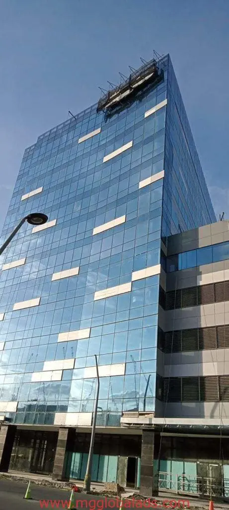 Modern building with reflective glass and gray panels, metallic signage in Ortigas, streetlamp and cones. By M&G Global Ads.