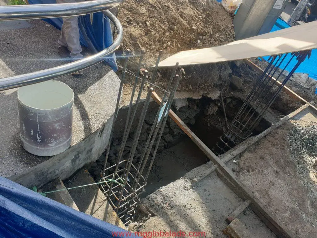Construction site with exposed rebar, hole, and safety signage in Makati. White bucket, railing, and worker visible by M&G Global Ads.