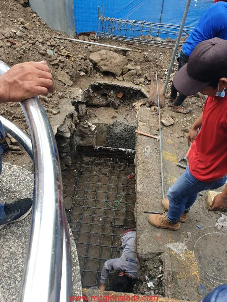 Workers build a concrete foundation with steel rebars near building signage in Makati by M&G Global Ads.