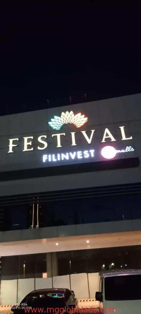 LED signage for Festival Filinvest Mall in Makati, brightly lit at night with colorful petal lights. Cars visible. By M&G Global Ads.