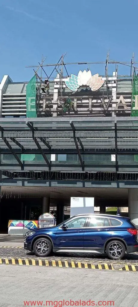 Metallic lotus flower business signage installation in Mandaluyong, workers on scaffolding, blue SUV outside—by M&G Global Ads.