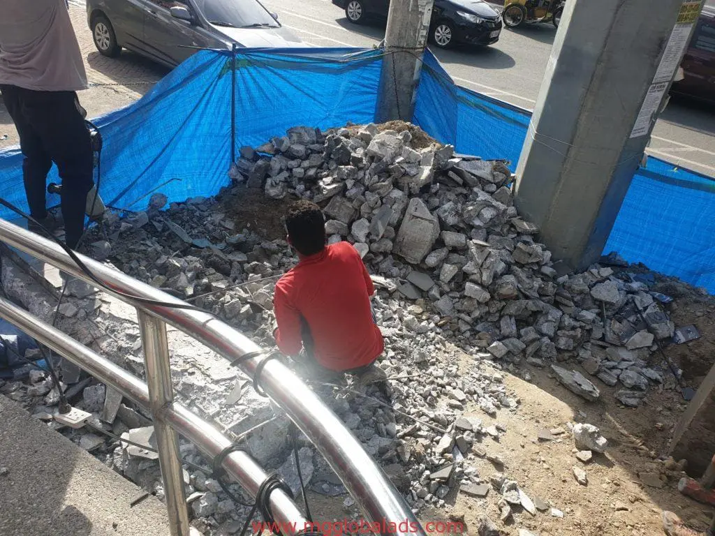 Building billboard signage installation in Mandaluyong, workers on site near blue tarp, cars passing—by M&G Global Ads.