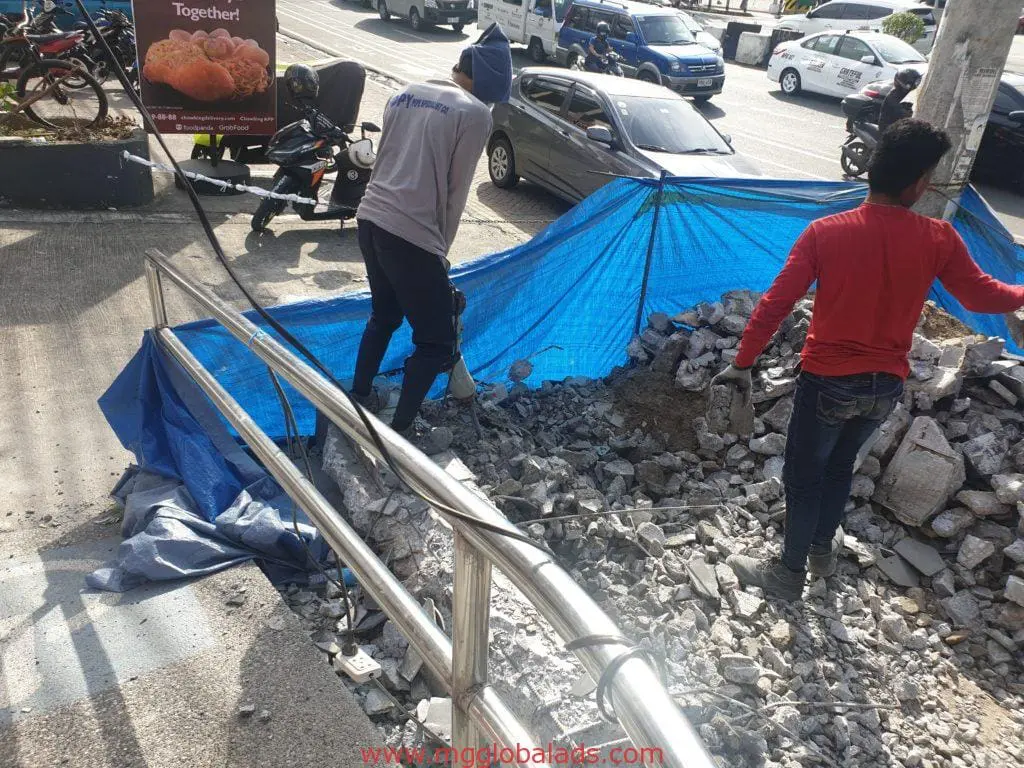 Workers clearing rubble on sidewalk, blue tarp, food billboard signage in Makati. Vehicles on road. By M&G Global Ads.