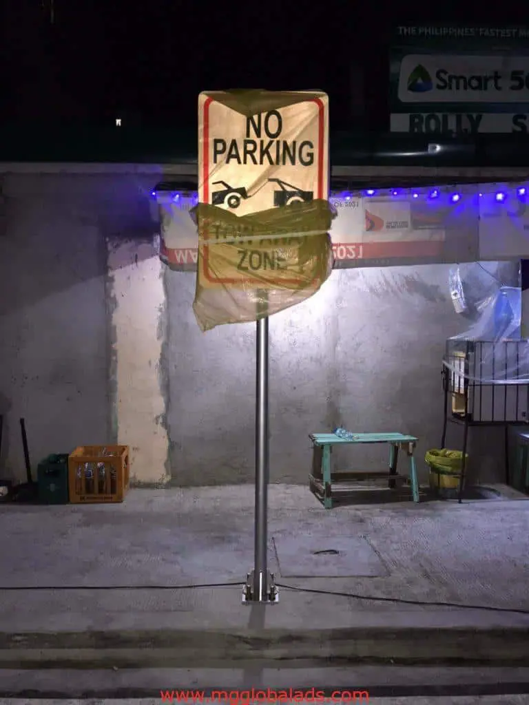 No Parking Tow Away Zone signage in Mandaluyong, partially wrapped, lit at night on quiet street by M&G Global Ads.