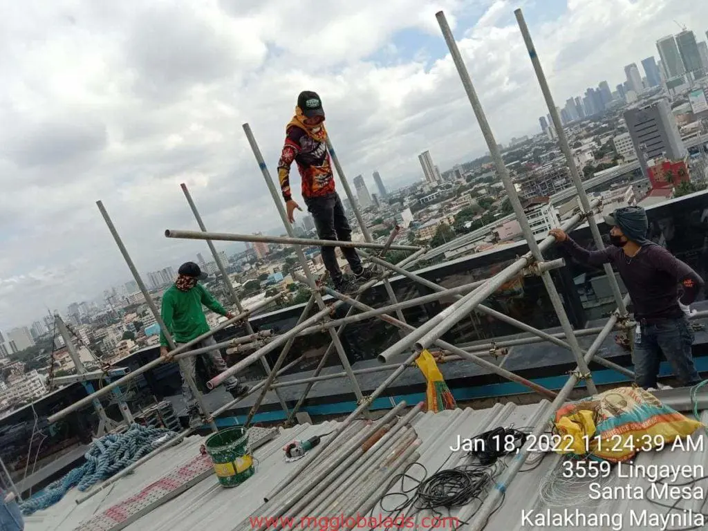 Billboard signage installation for a commercial client in Makati, with cityscape background; workers on scaffolding by M&G Global Ads.