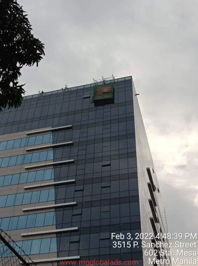 Acrylic office signage on high-rise with green platform, cloudy sky, Pasig location overlay by M&G Global Ads.