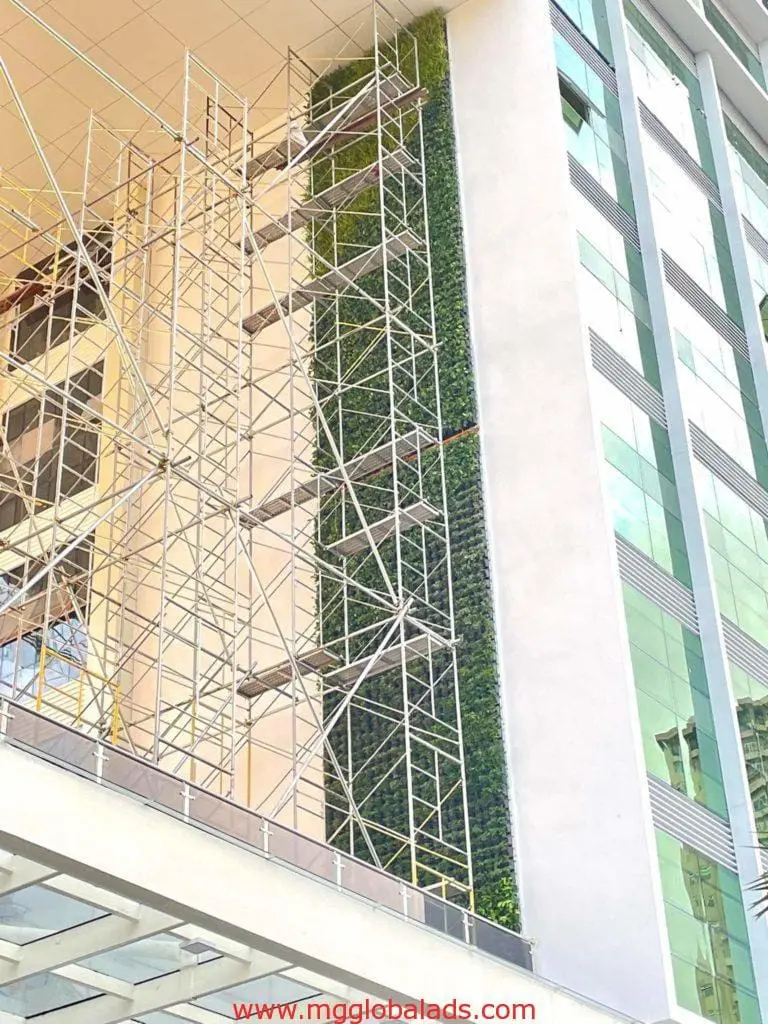 Modern pylon signage on a tall glass building under construction in Makati, with green wall and scaffolding, by M&G Global Ads.