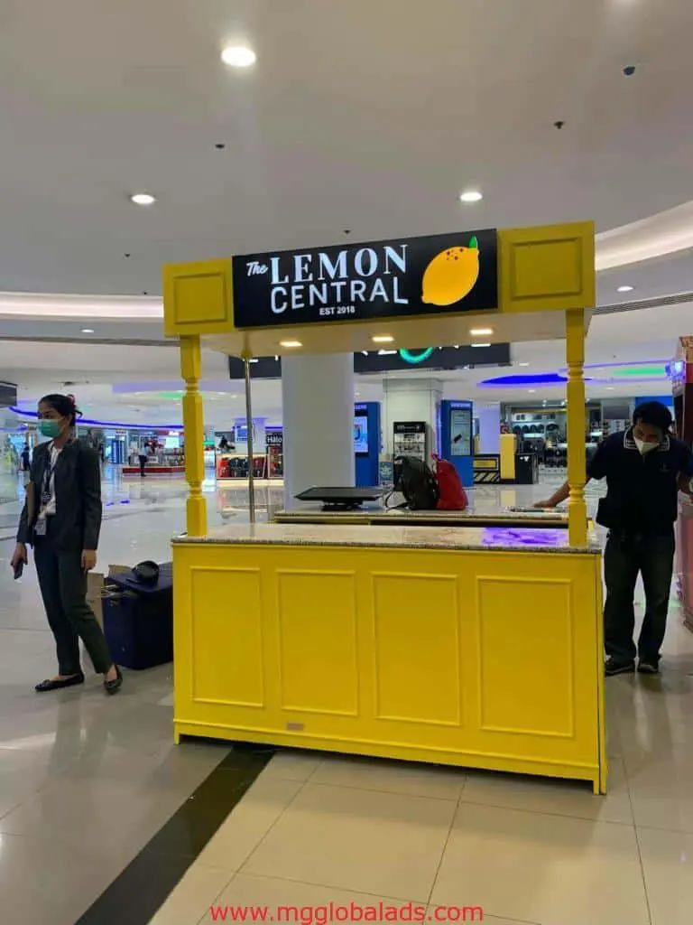 Building signage for The Lemon Central EST 2016 kiosk in a Makati mall by M&G Global Ads, with masked shoppers and stores visible.