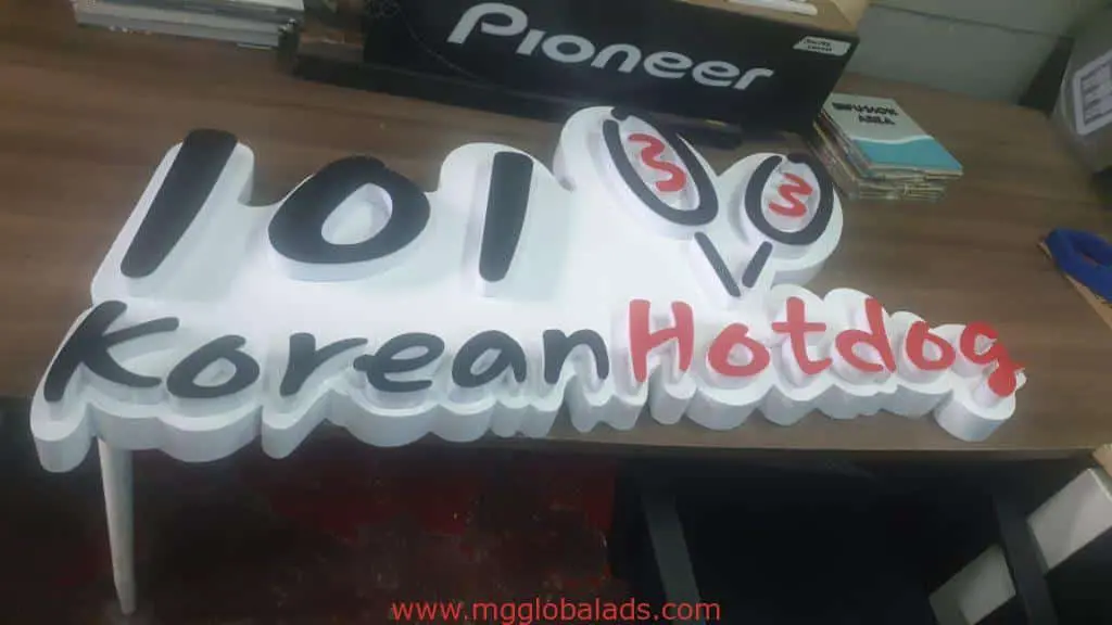Acrylic signage for 101 Korean Hotdog in Quezon City on table, stylized hotdog logo; Pioneer box in background. By M&G Global Ads.