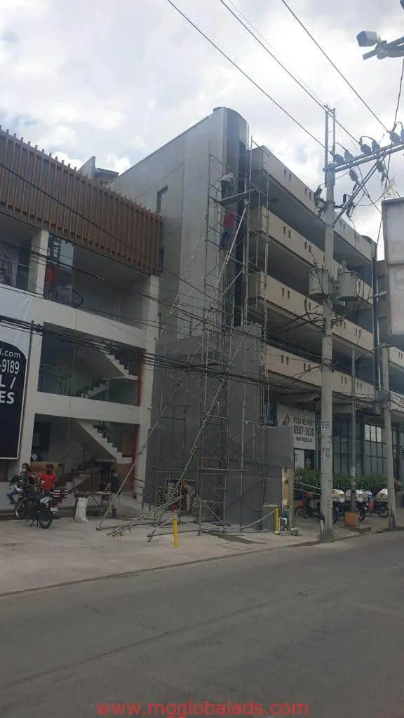 Acrylic building signage installation near motorcycles and workers in Ortigas, Metro Manila by M&G Global Ads.