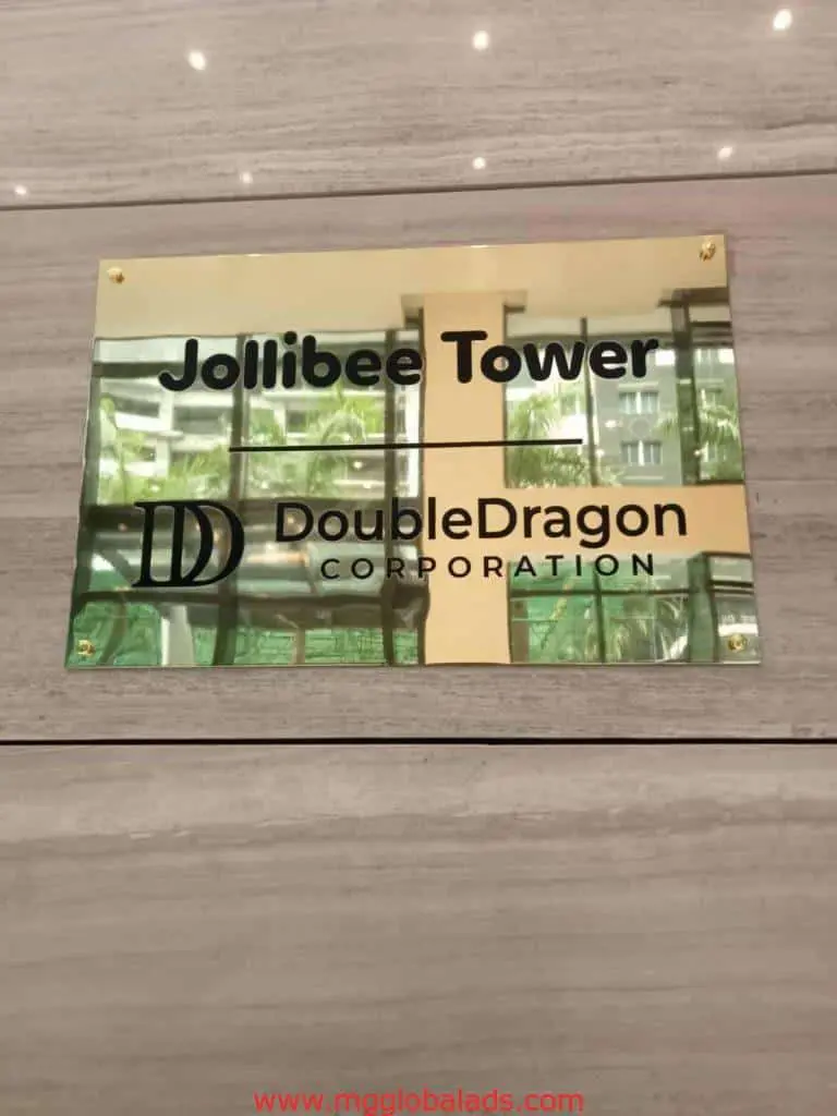 brass engrave building signage for Jollibee Tower and DoubleDragon Corporation in Ortigas, reflecting windows and greenery, by M&G Global Ads.