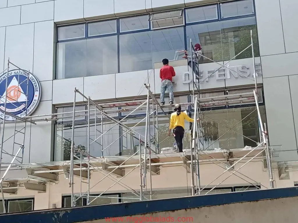 Workers installing aluminum signage for Office of National Defense, Makati, on scaffolding. Project by M&G Global Ads.