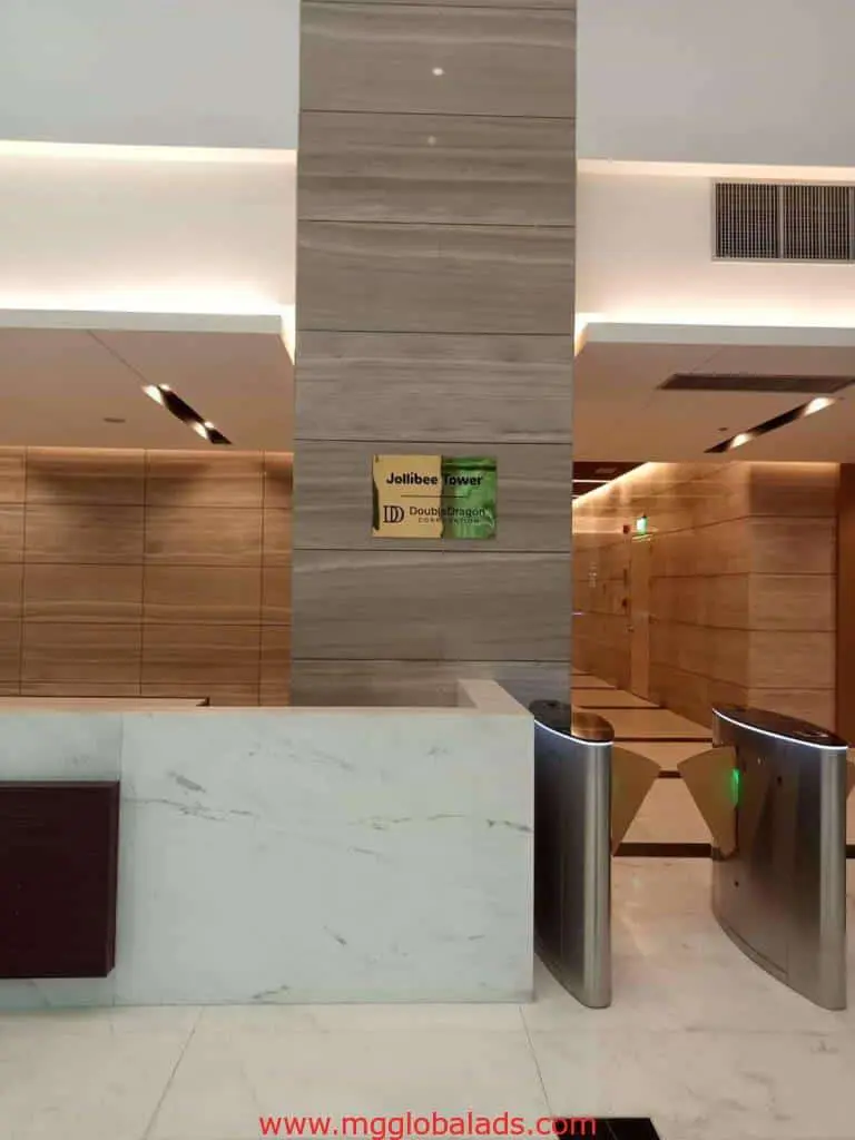 Acrylic signage for Jollibee Tower lobby in Ortigas with marble, wood paneling, and reception desk by M&G Global Ads.