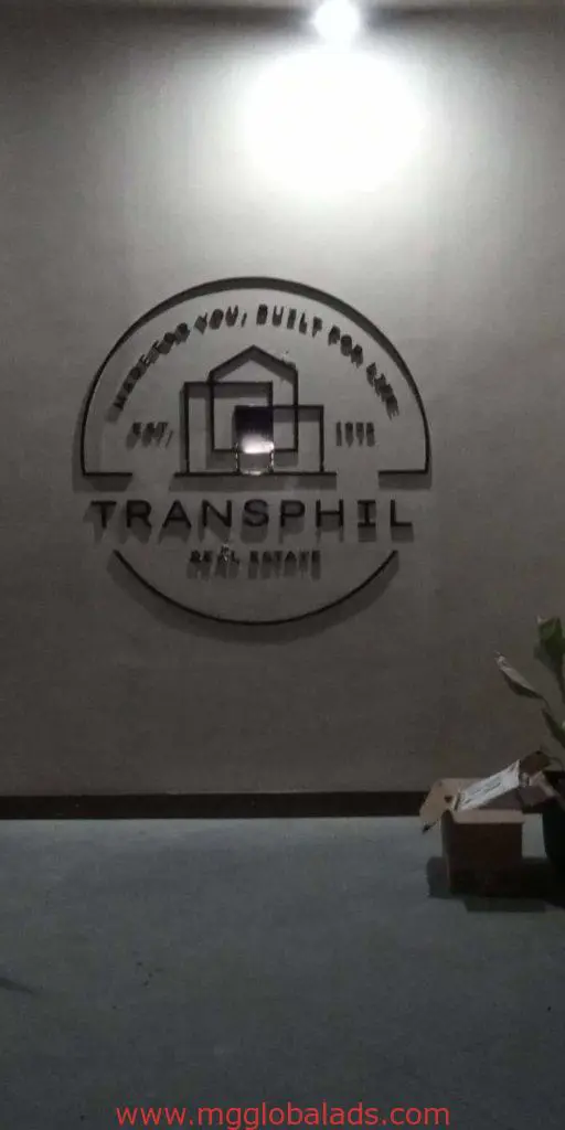 Illuminated metallic outdoor signage for TRANSPHIL in Makati, with logo. Cardboard box and plant below. By M&G Global Ads.