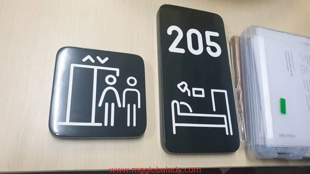 Black metallic hotel signage with elevator and room number 205 icons in Makati, paperwork on desk by M&G Global Ads.
