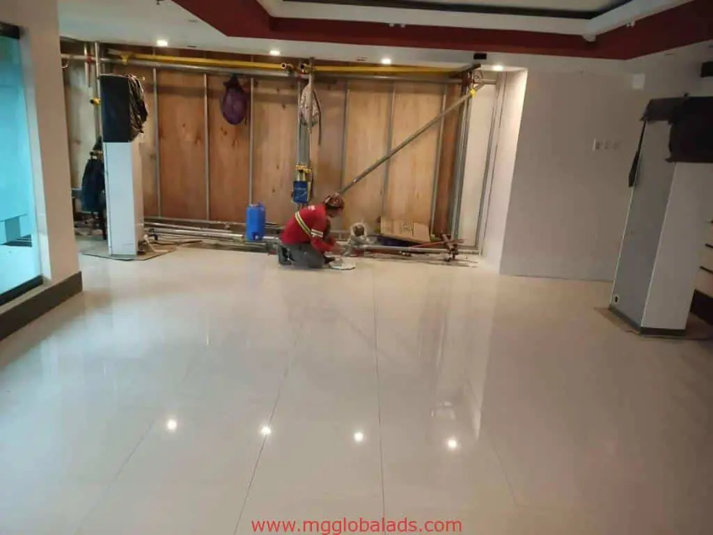 Worker inspects indoor wayfinding signage install for client in Mandaluyong by M&G Global Ads, shiny floor, exposed pipes.