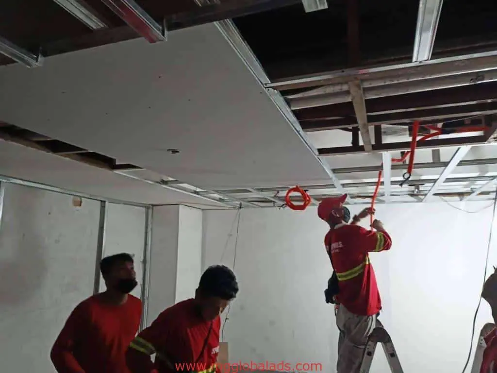 Workers installing drywall panels on ceiling with visible metallic sign in Makati office under construction by M&G Global Ads.