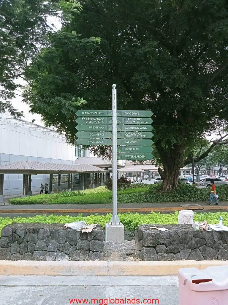 Directional metal signpost with green outdoor signage on a sidewalk in Quezon City, by M&G Global Ads.