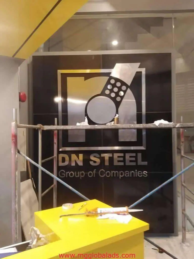 Metallic signage for DN STEEL Group of Companies at a construction area in Makati by M&G Global Ads. Scaffolding, tools, yellow counter.