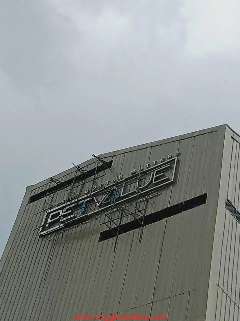 Damaged metallic PET VALUE building sign with missing letters, Ortigas location, overcast sky, by M&G Global Ads.