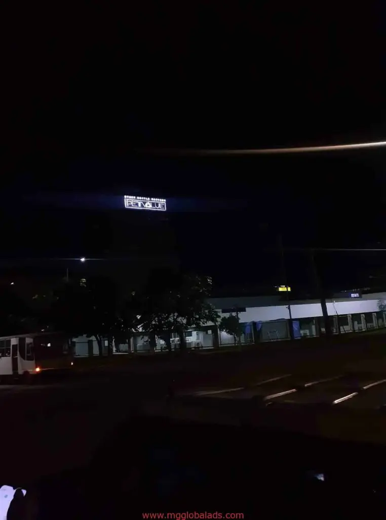 LED billboard signage above a building at night in Ortigas, with trees and a parked bus, by M&G Global Ads.