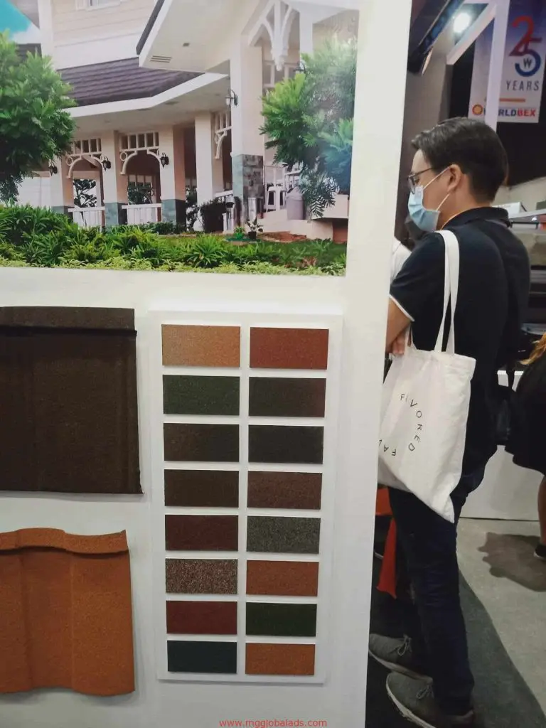 Metal signage display at a roofing material exhibit in Mandaluyong, with samples and a man wearing glasses, by M&G Global Ads.