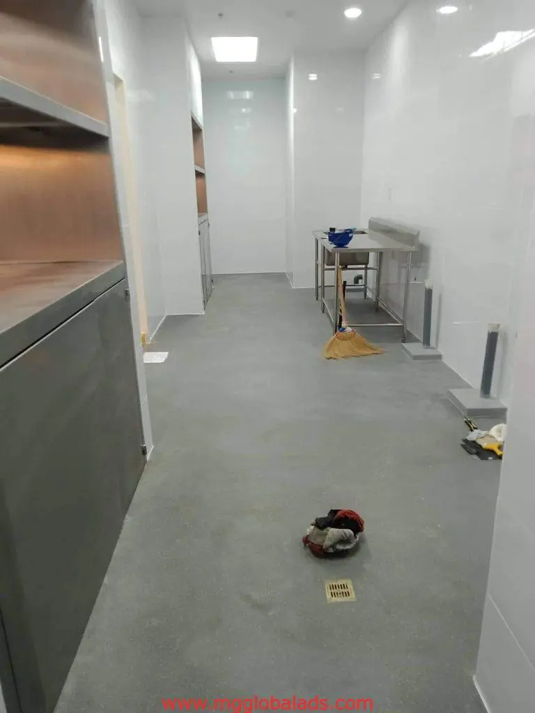 Commercial kitchen with shelves, metal table, cleaning supplies, and acrylic signage by entrance in Makati by M&G Global Ads.