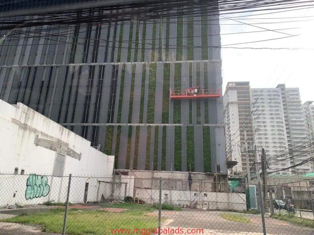 Workers install Greenwall and Moss Wall building in Mandaluyong—site fenced, debris visible—by M&G Global Ads.