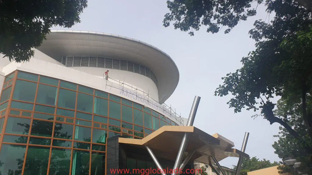 LED signage installation on modern building with green glass in Ortigas, worker on scaffolding near rooftop by M&G Global Ads.