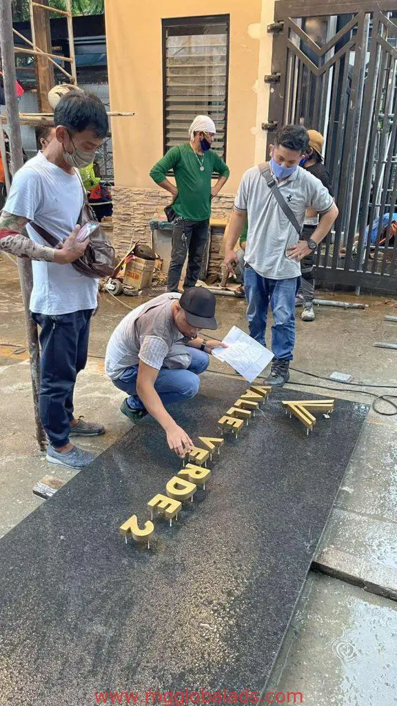 Team installs custom golden metal letter signage on black stone slab outside building in Makati, by M&G Global Ads.