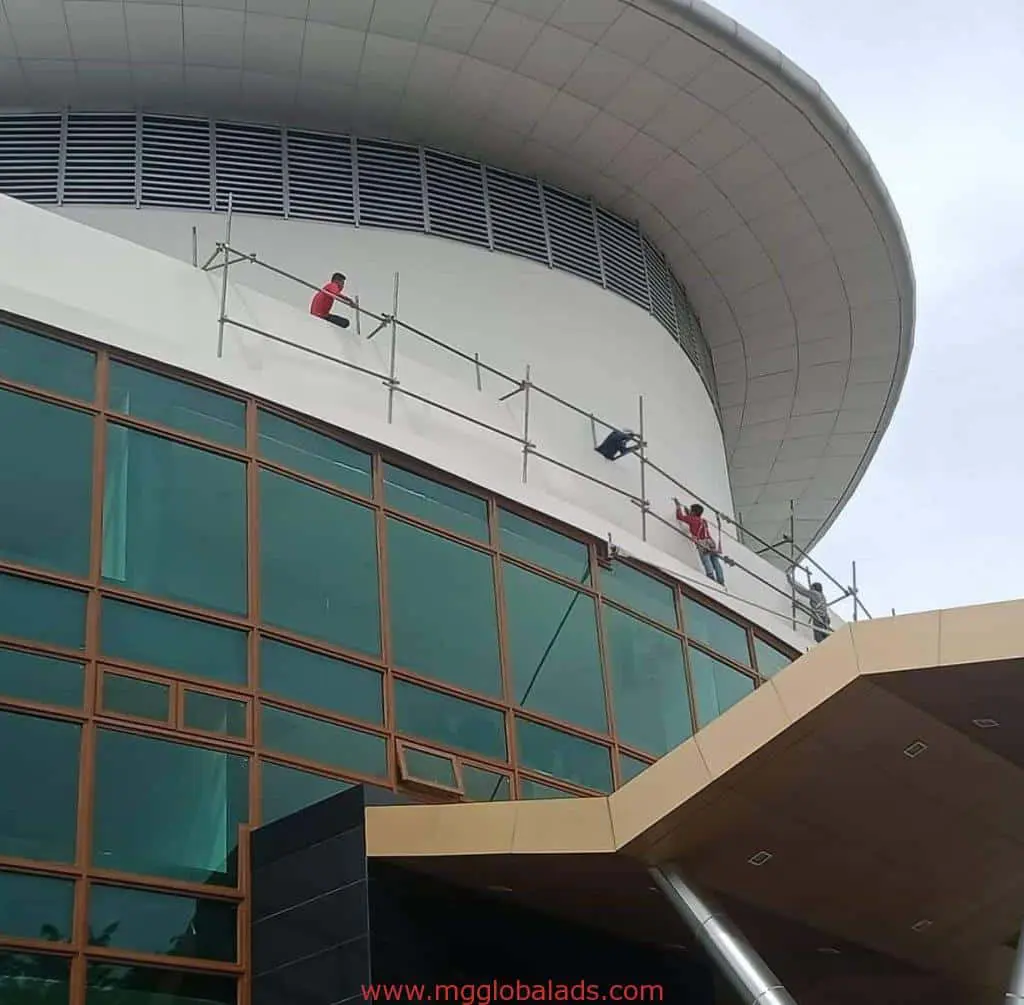 Workers installing acrylic building signage on a modern glass building in Ortigas, Metro Manila by M&G Global Ads.