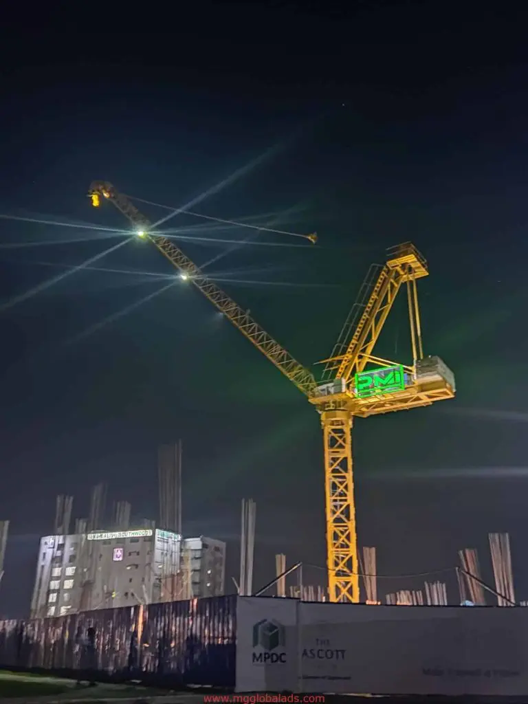 LED signage and construction crane illuminated at night in Makati building site, steel rods and lit building visible, by M&G Global Ads.