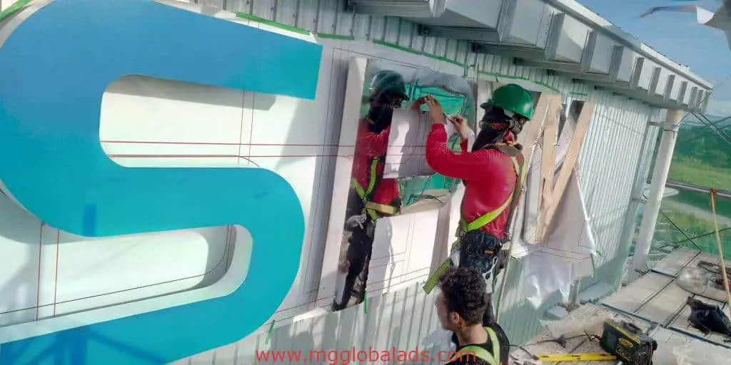 Acrylic channel letter signage installation at a Makati building, two workers in safety gear on-site by M&G Global Ads.