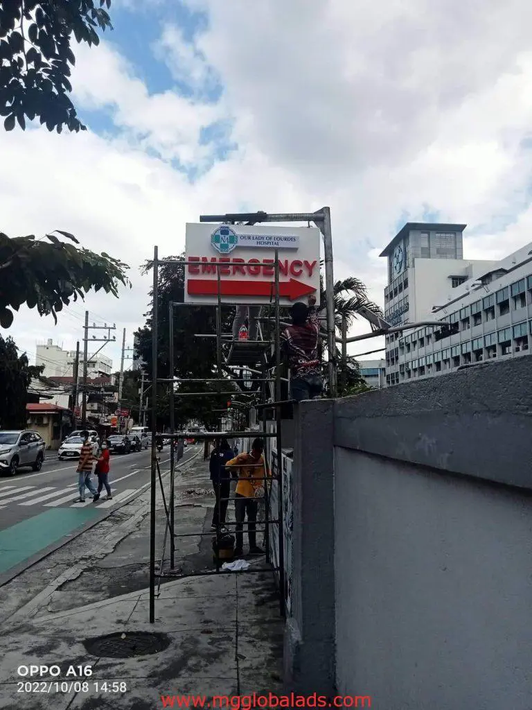 Hospital emergency outdoor metal signage installation in Mandaluyong, workers on scaffolding, by M&G Global Ads.