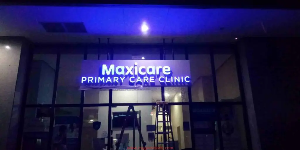 LED signage for Maxicare Primary Care Clinic in Quezon City, above glass doors at night, ladder and tools below, by M&G Global Ads.