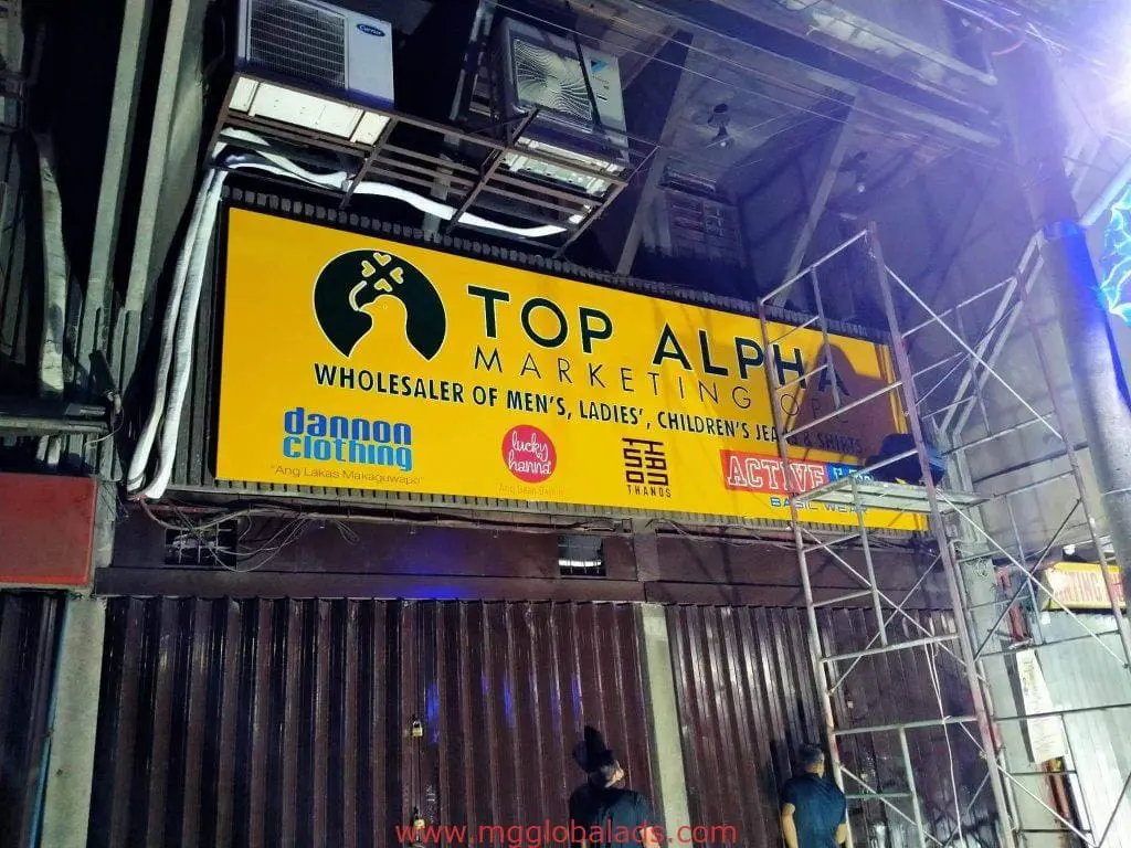 Top Alpha Marketing yellow LED signage in Quezon City for wholesale clothing, with brand logos and workers below by M&G Global Ads.