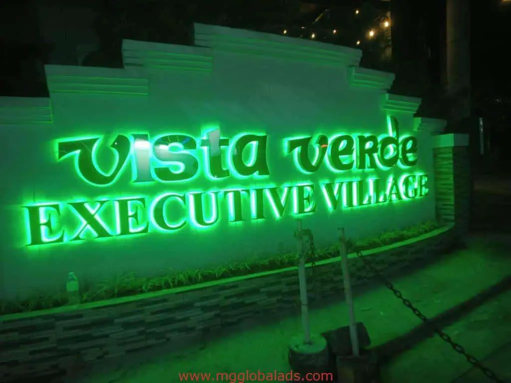 Neon green LED signage for Vista Verde Executive Village on a stone wall at night in Quezon City by M&G Global Ads.