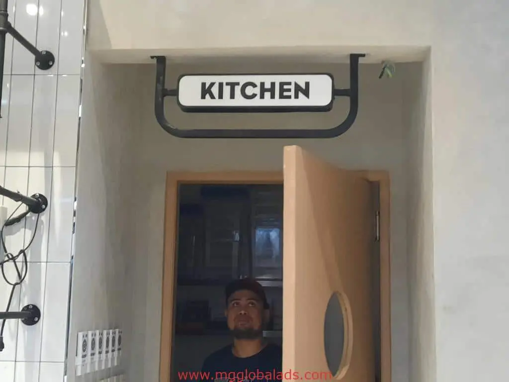 Metallic KITCHEN signage above doorway with man standing below, wooden door beside him, Ortigas location by M&G Global Ads.